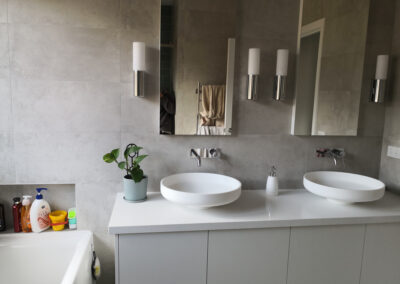 bathroom with circular basins, 2 mirrors, 4 lights, and in built shelf above bathtub