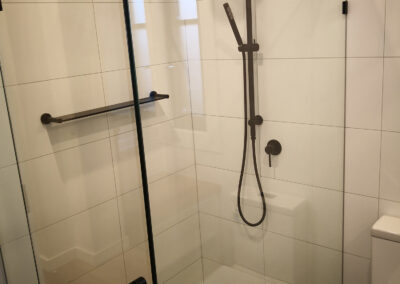 white tiled shower with black accents, including shelf, handle, shower head and tap