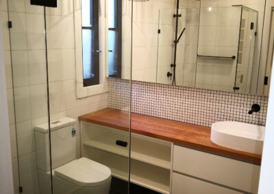 decorative splashback, mirror cabinetry on wall, one sink, wooden benchtop, toilet and shower, with decorative pendant light