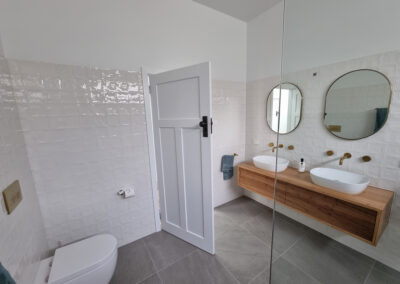 bathroom with wooden vanity looking from over bathtub, golden accent, including around mirror, taps and faucets, and toilet buttons