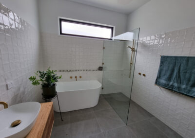 bathroom with wooden vanity looking toward bathtub, with gold accents, taps faucets, shower heads etc...