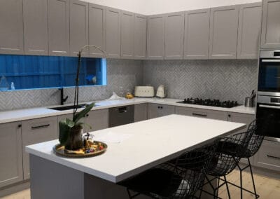 grey kitchen bench with white benchtop and black stools