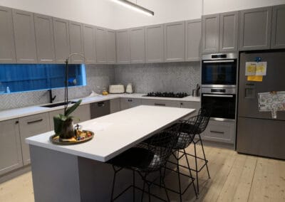 grey kitchen bench with white benchtop and black stools, grey cabinetry